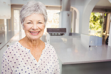 Smiling senior woman standing in modern kitchen, showing island countertop and range hood