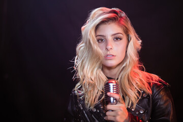 Female singer is holding vintage microphone in dim studio with white key light and red backlight