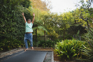 Boy jumping on in-ground trampoline in lush backyard garden, surrounded by ferns and shrubs
