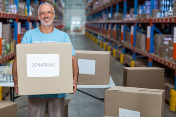 Male volunteer holding cardboard donation box in warehouse aisle, with folding table and shelving