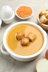 Delicious lentil cream soup served with croutons on light grey table, closeup