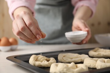 Woman putting salt onto raw pretzels at white wooden table, closeup