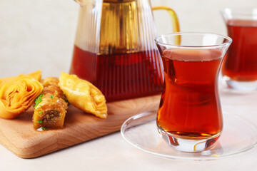 Traditional Turkish tea in glass cups, teapot and fresh baklava on white table, closeup