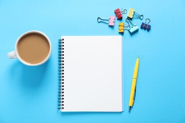 Open blank notebook, other stationery and coffee on light blue background, flat lay