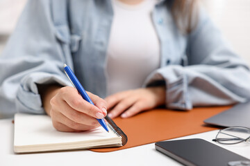 Woman writing in planner at white desk indoors, closeup
