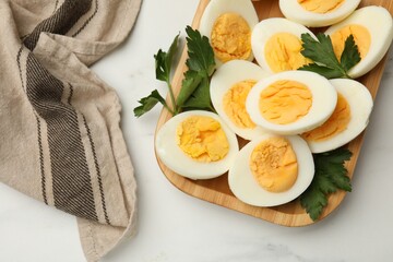 Boiled eggs and parsley on white marble table, top view