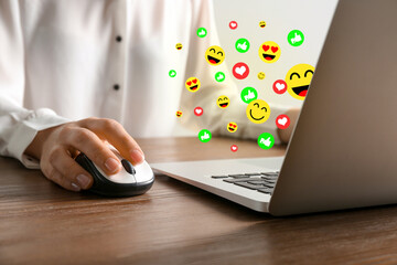 Woman using laptop at table, closeup. Social media notifications (likes and emojis) flying out of computer