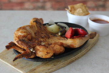 A whole grilled chicken served on a sizzling hot plate alongside vegetables, inviting a dining experience that promises savory flavors and a hearty meal perfect for gatherings.