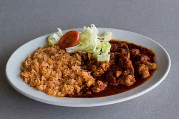 A vibrant plate featuring succulent pork asado in a rich sauce, paired with fluffy rice, garnished with fresh lettuce and tomato for a mouthwatering culinary delight.