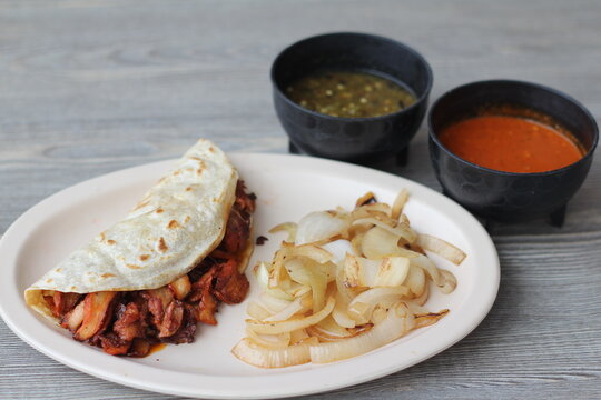 A vibrant plate of grilled gringa tacos filled with spiced meat, garnished with caramelized onions, complemented by a selection of delicious sauces for a satisfying meal experience.