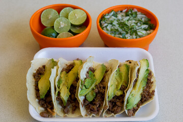 A delightful assortment of tacos loaded with meat and avocado, served alongside lime wedges and fresh onion-cilantro mix, presenting vibrant colors and textures.