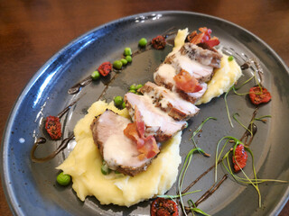 Danish - An elegant appetizer dish featuring sliced pork tenderloin on mashed potatoes, garnished with baked tomatoes, peas, and crispy bacon.