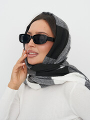 Young woman poses with scarf and sunglasses in stylish indoor setting