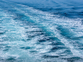 Fototapeta premium 快晴の空と穏やかな海の海上、船舶のスクリューの泡の跡、白とブルーのグラデーションと細かい泡のラインが綺麗です。船跡は右側から左側奥に斜めに流れるラインで横構図です。