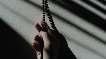 Hand holding rosary beads in shadowy light. Christian prayer and meditation. Symbolic image for Lent, Holy Week, Good Friday, Easter season