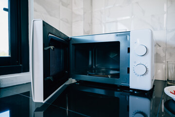 An open microwave oven door on a sleek kitchen tabletop presenting modern technology and design in...