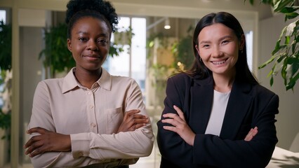 Confident businesswomen business partners multiracial women African Asian colleagues American Chinese girls professional employees co-workers hands crossed posing together looking smiling in office