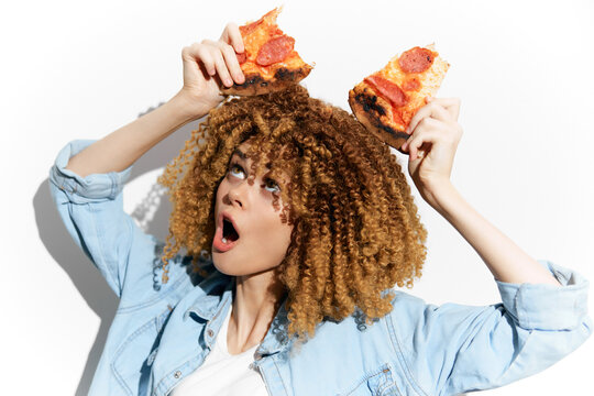 A joyful woman with curly hair holding slices of pepperoni pizza, expressing excitement and love for food, ideal for concepts like indulgence and pizza appreciation
