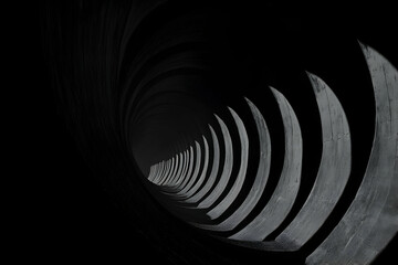 Obraz premium Abstract grayscale image of a spiraling concrete tunnel, leading to a distant light source. The image evokes feelings of mystery and depth.