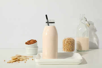 Bottles of alternative milk and herbal ingredients on light background