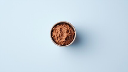 A small bowl filled with cocoa powder on a light blue background, viewed from above.