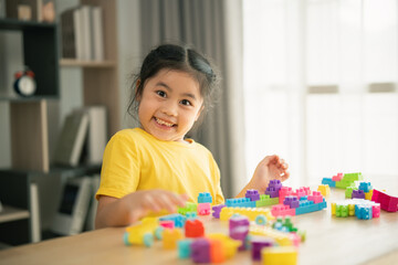 Fototapeta premium Happy young girl playing with colorful building blocks in a bright and cheerful room, showcasing creativity and joy in childhood playtime