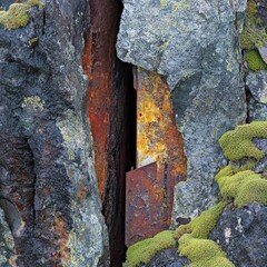 Weathered rock face with a rusted metal fragment wedged between stones, accented by patches of vibrant green lichen
