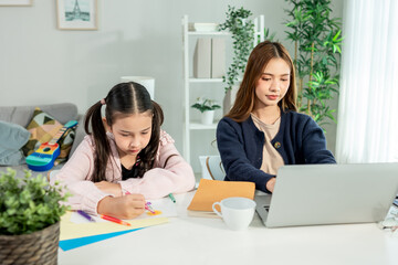 Asian attractive mother working from home while daughter doing homework