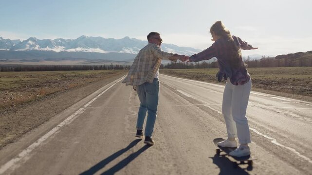 Young couple learning to ride a longboard together on a scenic mountain road.