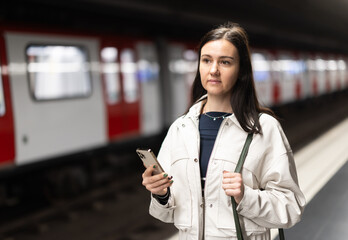 Woman stands with mobile phone at subway station
