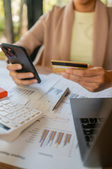 Close-up of hands holding a smartphone and credit card over financial documents, showcasing online business transactions.