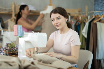 Female seamstress is sitting near sewing machine and create new dress in the workshop