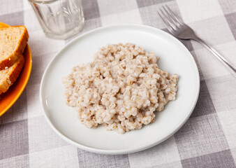 There is portion of freshly prepared pearl barley porridge in plate. Traditional dietary European breakfast.