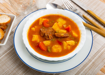 Delicious stewed pork in sauce with potatoes and vegetables on plate. Traditional spanish dish patatas estofadas con carne