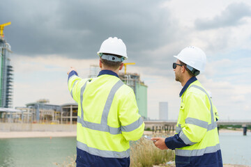 Engineering team in safety gear planning pipeline maintenance at oil and gas refinery site with storage tanks in the background.