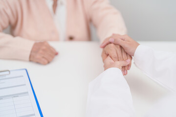 doctor holding hands with elderly female patient, showing empathy and support during a medical...