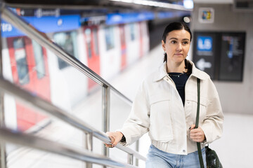 Naklejka premium Woman metro passenger climbs stairs, enters underground public transport station, moves on escalator, stands on moving steps.
