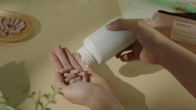 One hand holds a bottle of dietary supplements and pours pills into the other hand. The brown pills are vitamin and nutritional supplements that are good for health. Top view with the back blurred.