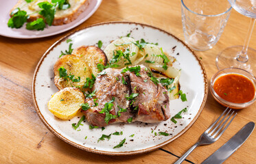 Juicy baked lamb chops accompanied by roasted potatoes and onion slices, topped with fresh herbs and served with side of red sauce for dipping..