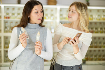 Girl customer and her female friend choose perfumes in store, and companion shows fragrances star fans on phone screen.