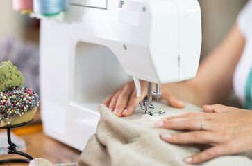 Female hands of seamstress sewing clothes on sewing machine in sewing workshop close-up