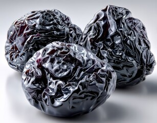Three Wrinkled Black Prunes on a Light Background, Highlighting Their Unique Texture and Color with a Soft Reflection for Culinary and Health Themes