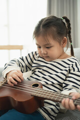 Fototapeta premium Young Child Playing Ukulele at Home, Indoor Scene Focused on Music, Creativity, and Joyful Learning in Natural Light with Warm Atmosphere