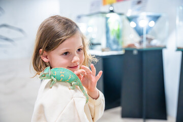 Little girl holding a green chameleon in her hands. Concept of childhood curiosity, interaction with exotic animals, and early interest in biology