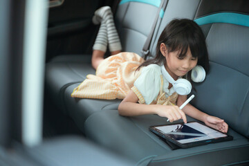 Child enjoys creative drawing in the backseat of a car during a family road trip in a sunny outdoor setting