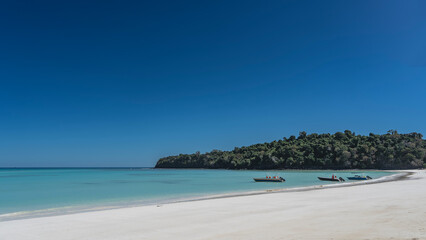 Beautiful tropical beach. White sand. A calm turquoise ocean. Motor boats are moored at the shore. A green hill against a clear blue sky. Madagascar. An idyll. Nosy Iranja. Copy space