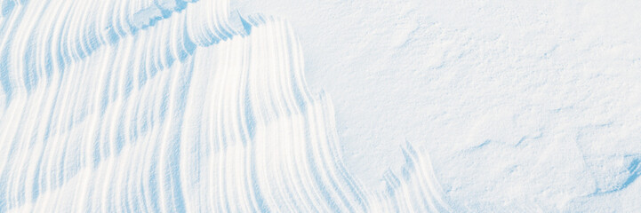 Obraz premium Wide panoramic winter background with snowy ground. Natural snow texture. Wind sculpted patterns on snow surface.