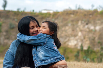 Fototapeta premium Latin american daughter embracing and kissing her mother outdoors
