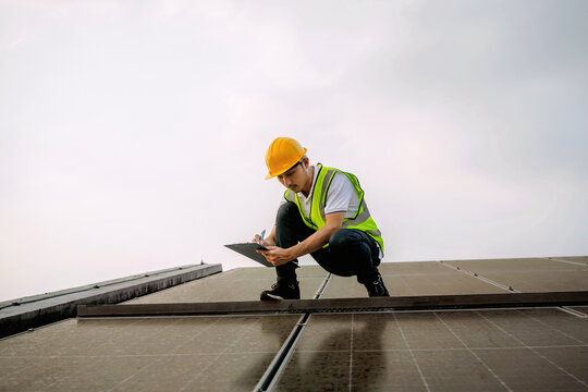 man in a yellow hard hat is writing on a clipboard while kneeling on a roof - Powered by Adobe
