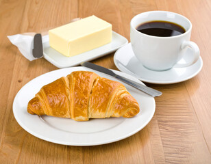 Freshly baked croissant with butter and cup of coffee on wooden table creates warm and inviting breakfast scene. golden pastry complements rich beverage perfectly